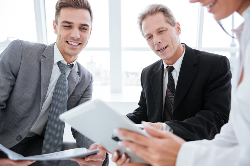 Cropped image of three business people sit with tablet computer in office. Focus on tablet